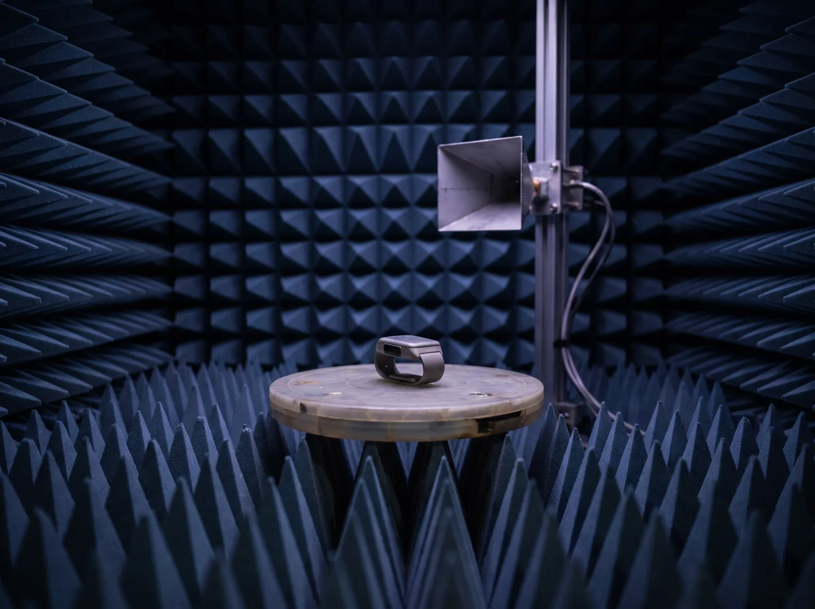 Illustration: a small wireless device on a turntable inside an RF test chamber lined with absorber cones
